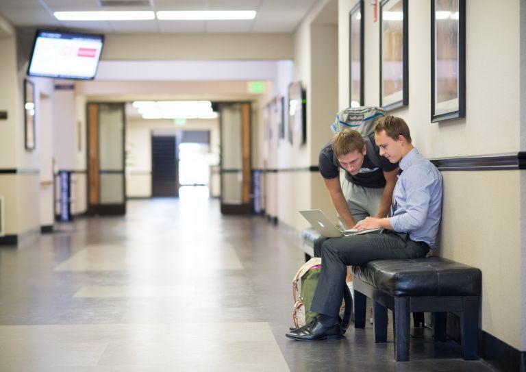 商学院学生在韦伯大厅的走廊里看着一台笔记本电脑