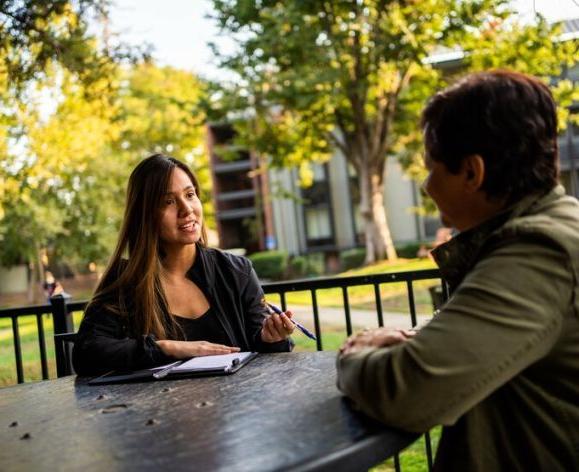 Photo shows two students talking at an outdoor table on the Sacramento campus.